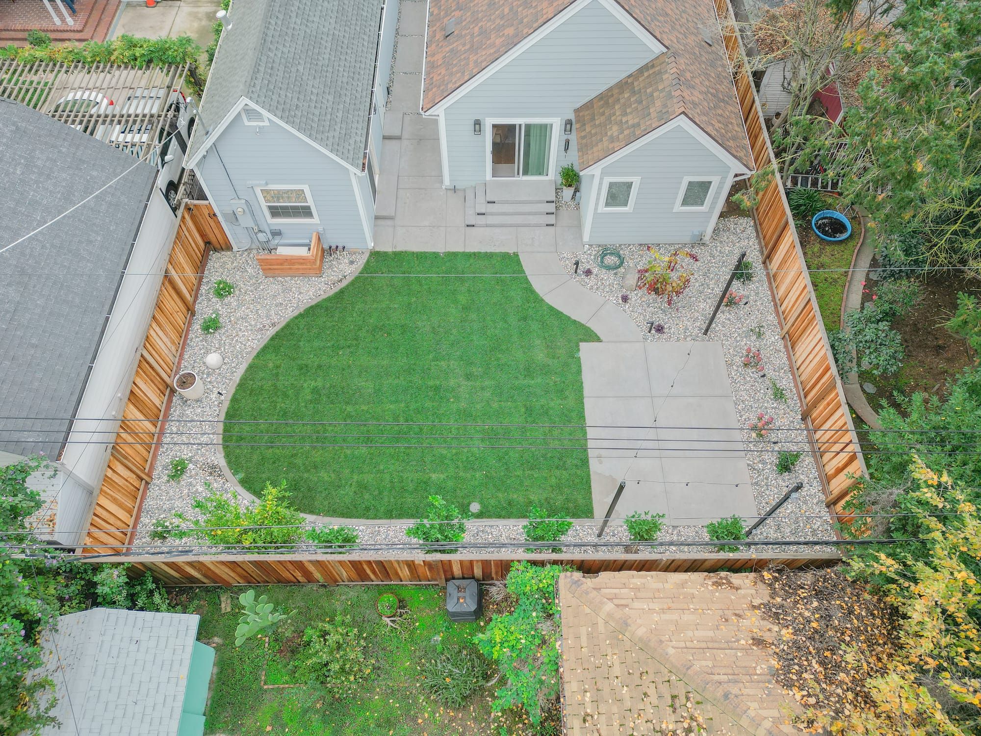 Aerial view of completed Sacramento backyard with concrete patio, curved sod lawn, gravel borders, and cedar fencing
