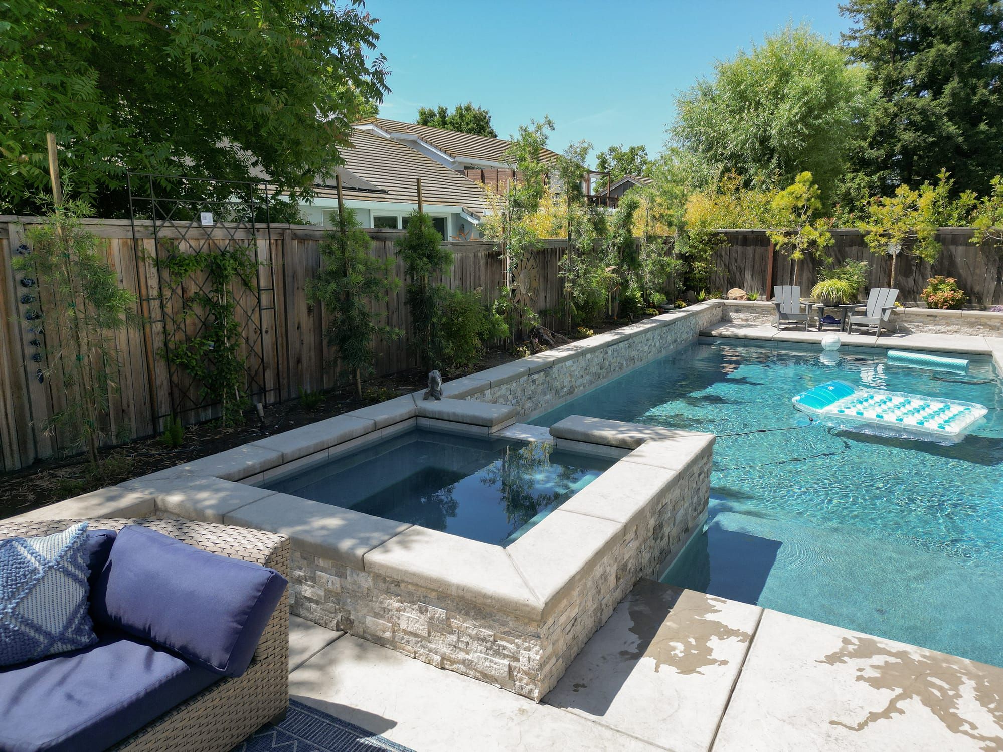 Backyard pool and spa with stone veneer walls, concrete coping, and patio seating in Sacramento