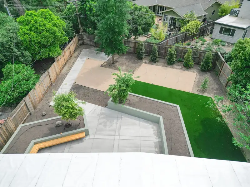 Aerial view of a backyard mid-build with soil graded and shaped, a new retaining wall, and finished concrete in place