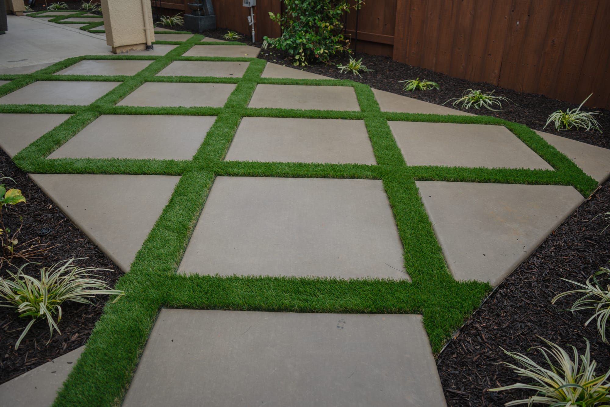 Concrete paver grid with artificial turf joints and mulch beds in Sacramento backyard